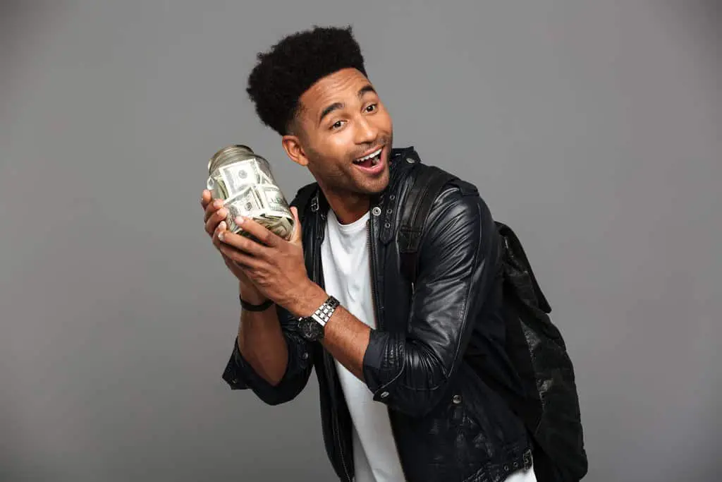 Handsome happy afro american man in leather jacket holding glass full of money