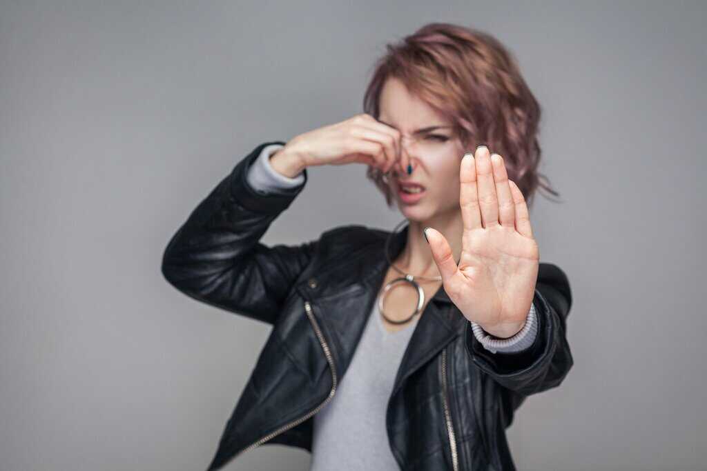 beautiful girl with black leather jacket standing pinching her nose and stoping bad smell.