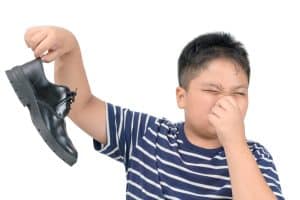 Disgusted boy holding a pair of smelly faux leather shoes