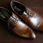Groom's leather shoes with creases on wooden floo
