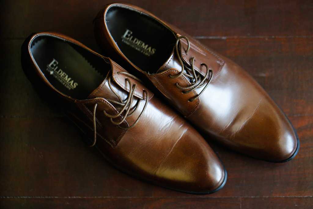 Groom's leather shoes with creases on wooden floo