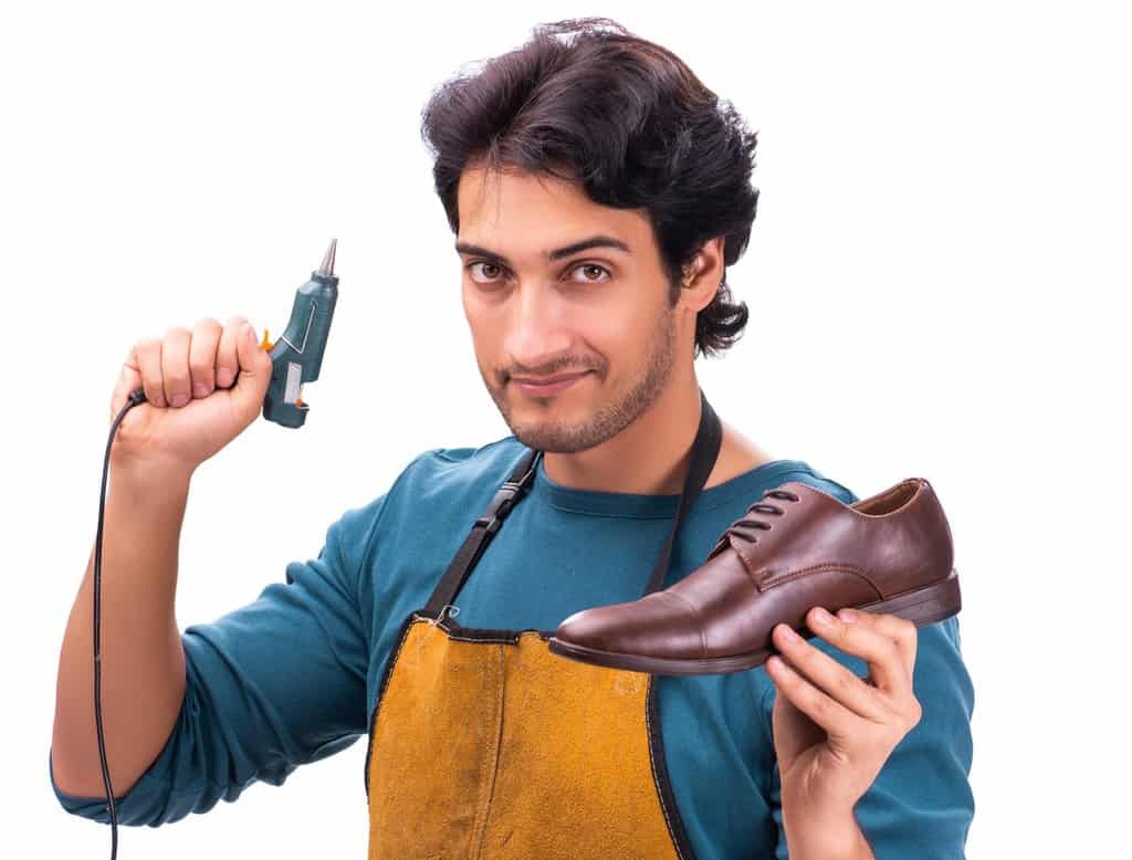 Young handsome shoemaker holding hot glue gun