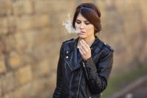 Beautiful woman in black leather jacket smoking weed outdoors