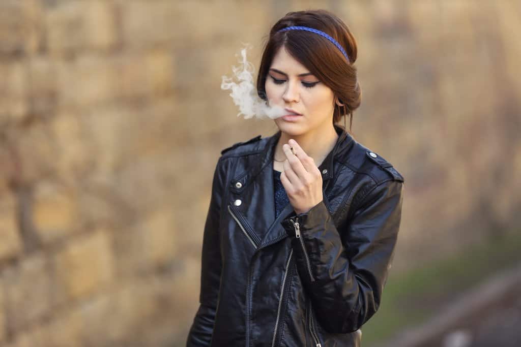 Beautiful woman in black leather jacket smoking weed outdoors
